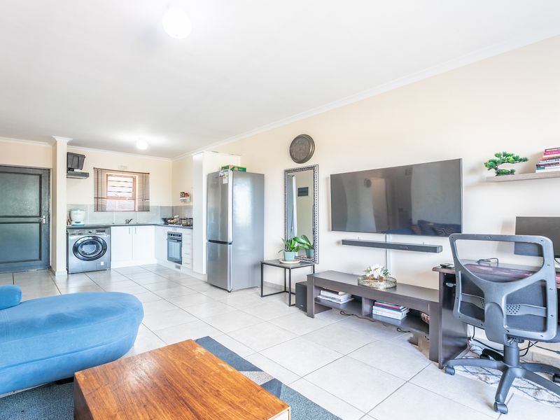 Open-plan living area featuring tiled flooring and a functional kitchen with built-in cabinetry, oven, and hob, creating a versatile and connected living space.