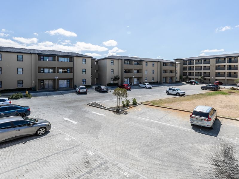 An elevated view of a modern apartment complex featuring paved parking areas and multi-story residential blocks with balconies.