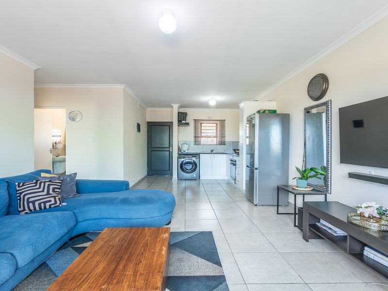 An open-plan living area featuring tiled flooring, a modern kitchen with built-in cabinetry, and integrated appliances, creating a functional and cohesive living space.