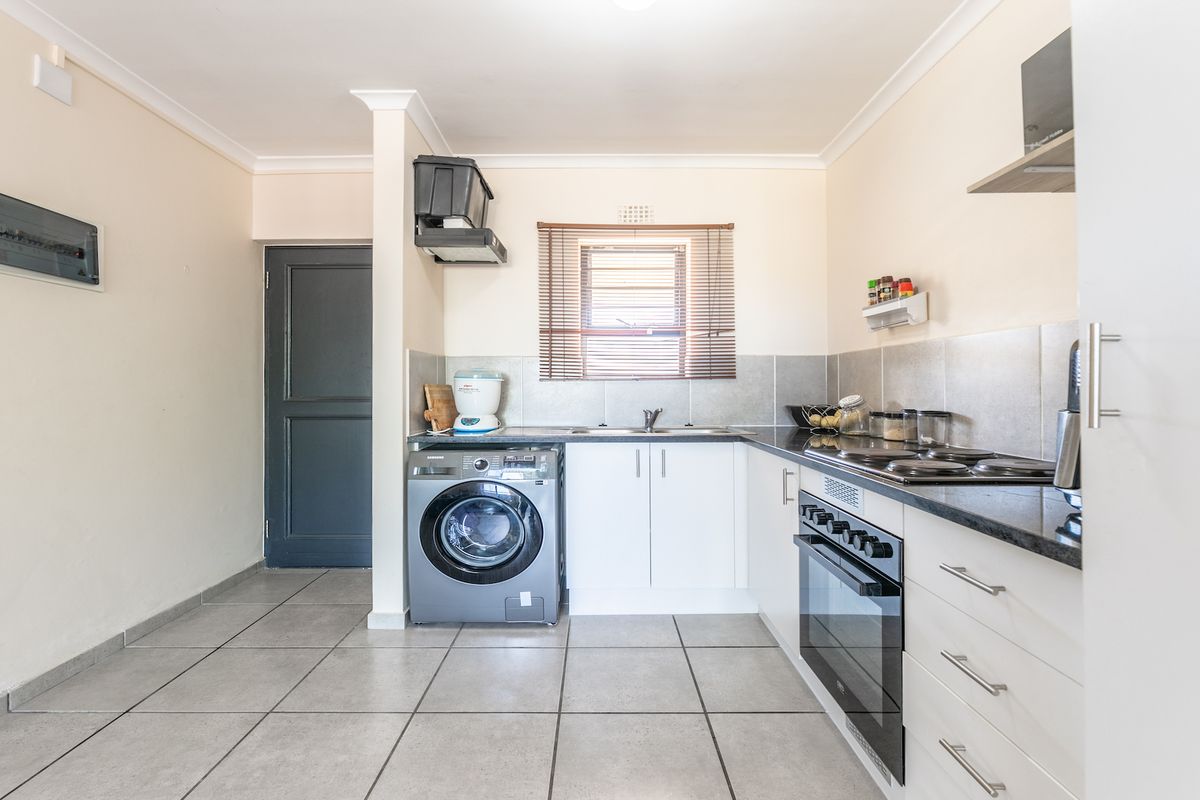 A functional kitchen featuring white cabinetry, dark countertops, tiled flooring, and integrated appliances including an oven and hob.