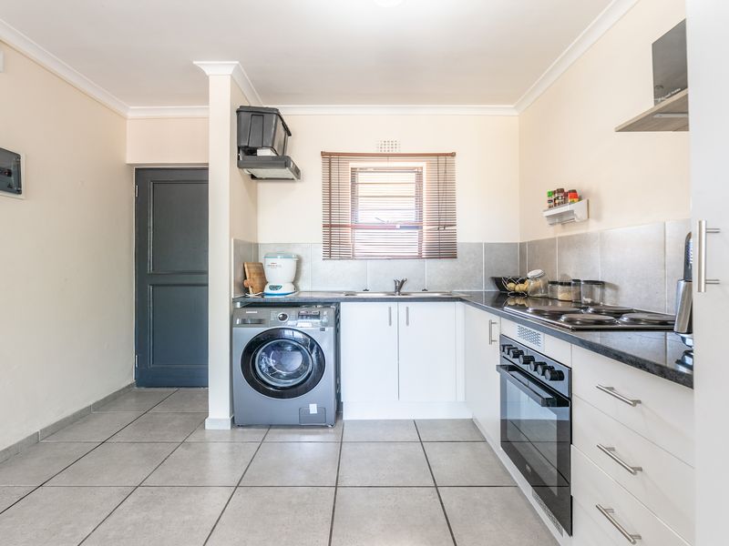 A functional kitchen featuring white cabinetry, dark countertops, tiled flooring, and integrated appliances including an oven and hob.