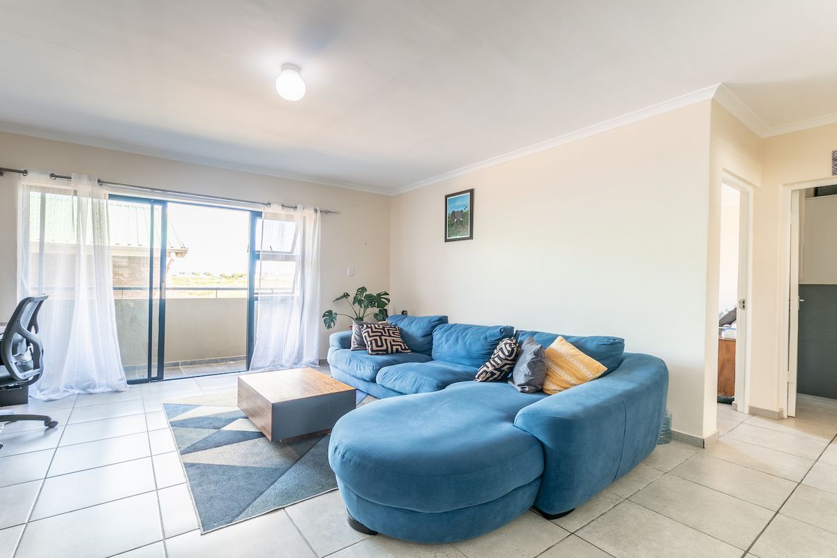 Spacious living room featuring neutral tiled flooring, cove cornicing, and large sliding glass doors providing direct access to an outdoor balcony area.