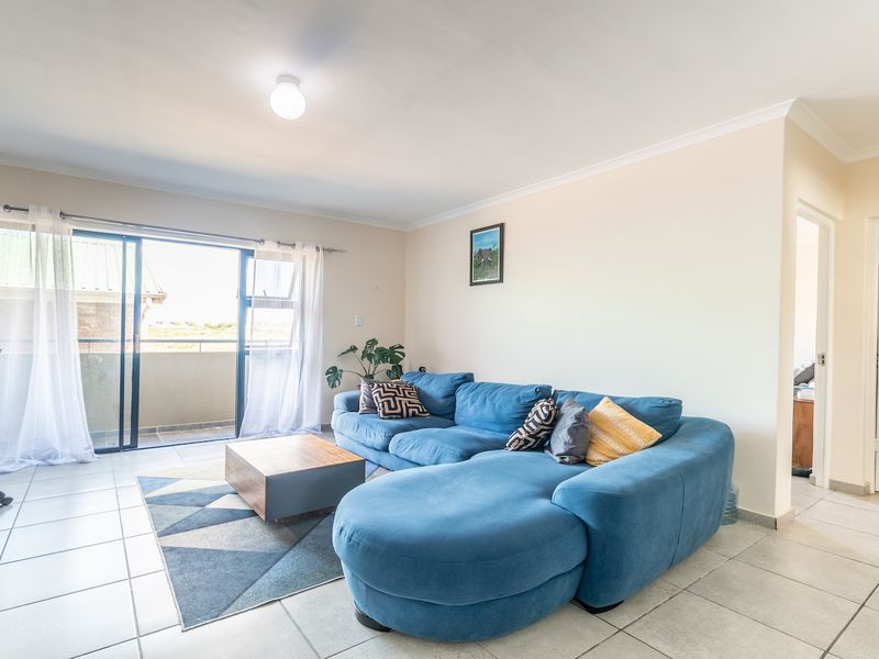Spacious living room featuring neutral tiled flooring, cove cornicing, and large sliding glass doors providing direct access to an outdoor balcony area.