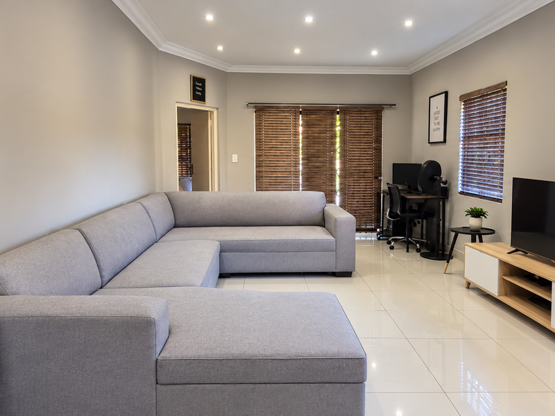 A well-maintained living room featuring neutral walls, tiled flooring, recessed downlighting, and wooden venetian blinds.