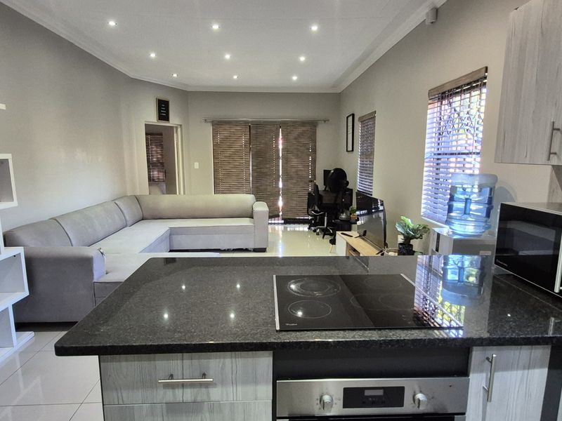 Modern open-plan living area featuring a well-appointed kitchen with granite countertops, built-in oven, and hob, flowing seamlessly into a spacious lounge with tiled floors.