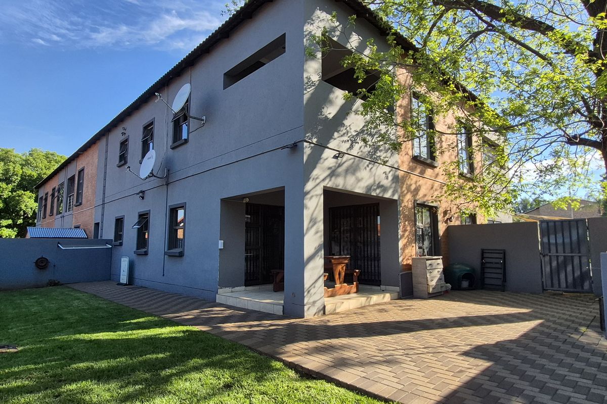 Rear view of a two-story townhouse featuring a paved patio area, landscaped lawn, and secure boundary walls with electric fencing.