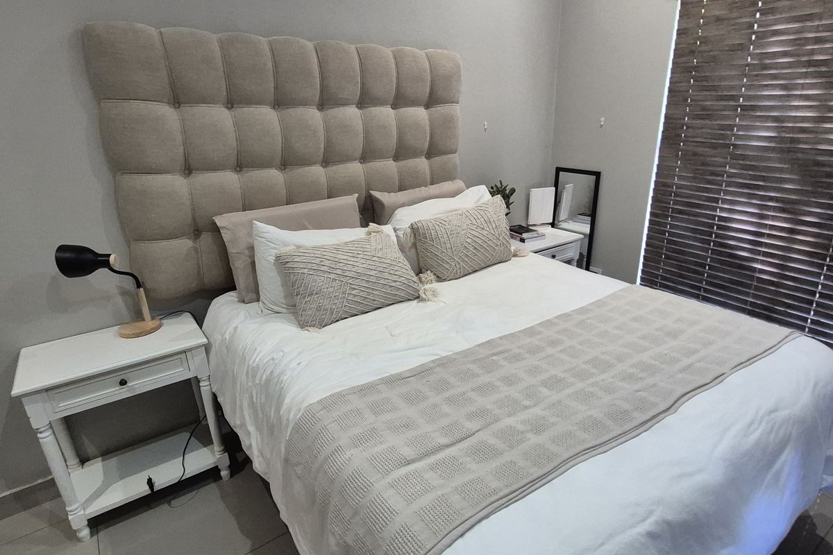 A well-maintained bedroom featuring neutral wall tones, tiled flooring, and fitted venetian blinds, providing a clean and comfortable living space.