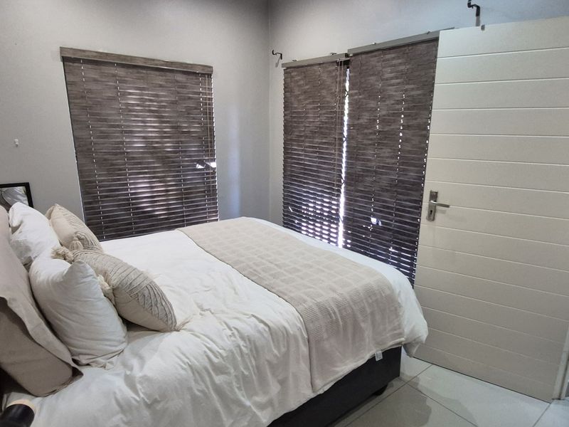 A well-maintained bedroom featuring tiled flooring, modern sliding door access, and fitted venetian blinds for privacy.