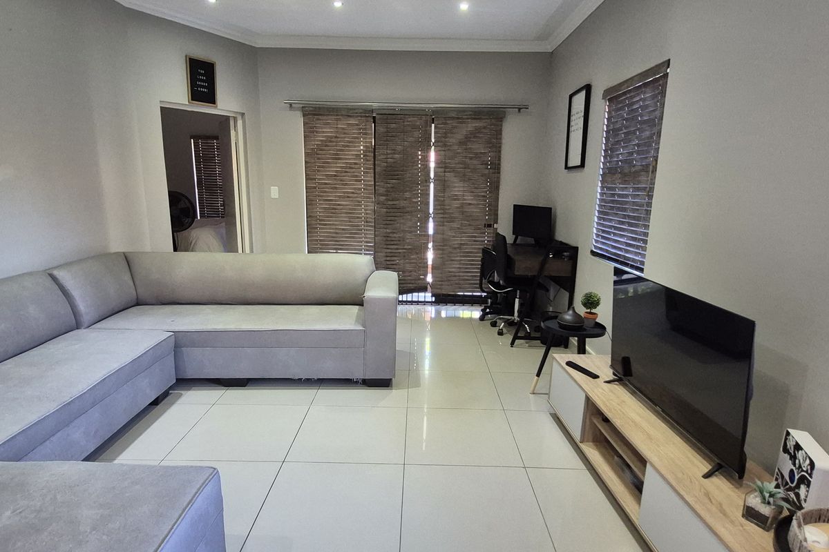 A well-lit living room featuring large format floor tiles, recessed ceiling lighting, and sliding door access to the exterior.