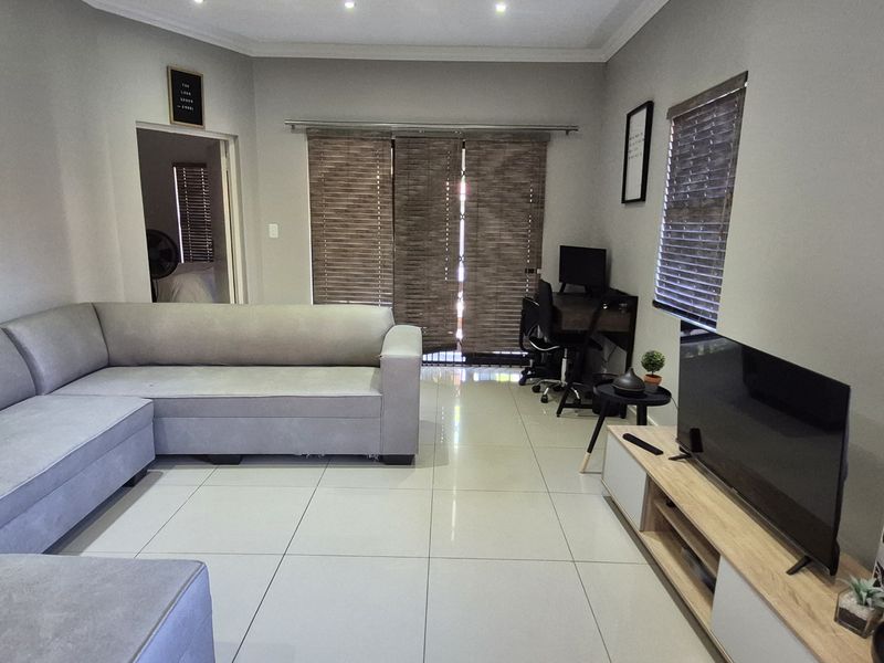 A well-lit living room featuring large format floor tiles, recessed ceiling lighting, and sliding door access to the exterior.
