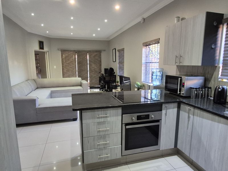 Modern open-plan kitchen and living area featuring contemporary cabinetry, stone countertops, integrated appliances, and sleek tiled flooring throughout.