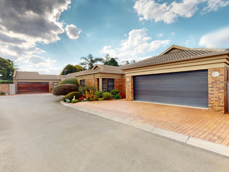 Front exterior view of a well-maintained brick house featuring a paved driveway, double garage, and landscaped garden area.