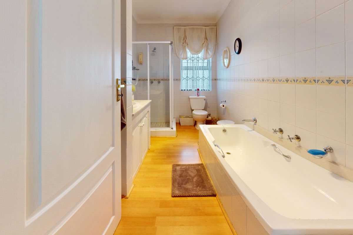 A functional bathroom featuring a bathtub, separate shower enclosure, built-in vanity, and wall tiling with laminate flooring.