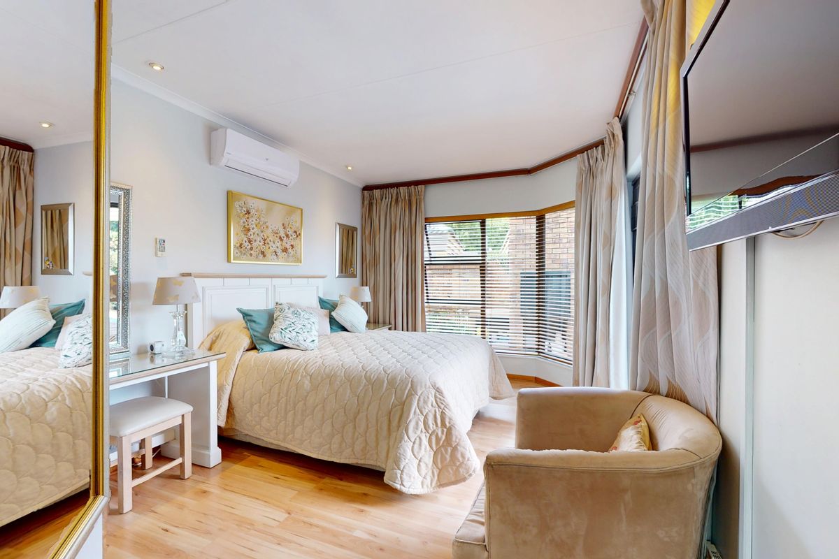 A well-maintained bedroom featuring timber flooring, a bay window, and a wall-mounted split-system air conditioner.