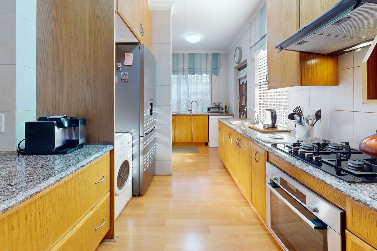 A functional galley-style kitchen featuring wooden cabinetry, granite countertops, a gas hob, and integrated oven, offering ample storage and workspace.