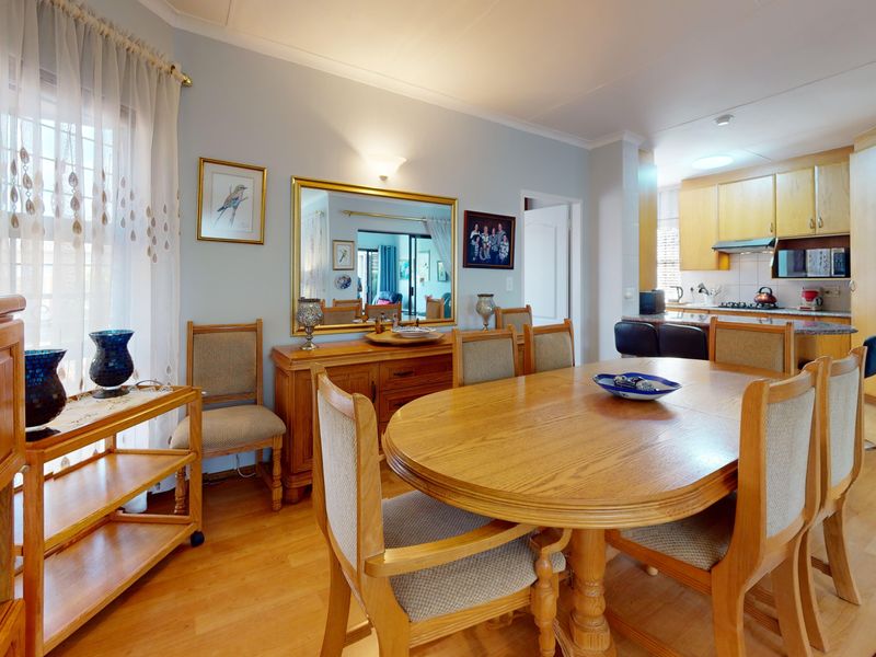 Open plan dining area flowing into a functional kitchen with wood-finish cabinetry, breakfast bar, and laminate flooring throughout.
