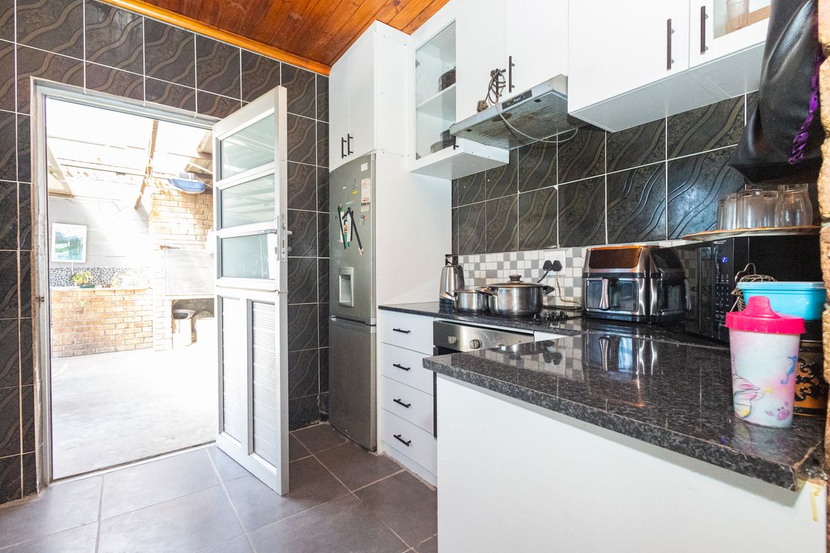 Compact kitchen featuring granite countertops, built-in oven, hob, extractor fan, and direct access to an outdoor patio area.