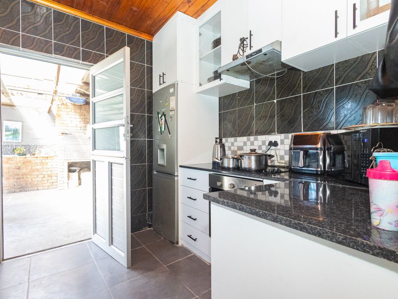 Compact kitchen featuring granite countertops, built-in oven, hob, extractor fan, and direct access to an outdoor patio area.