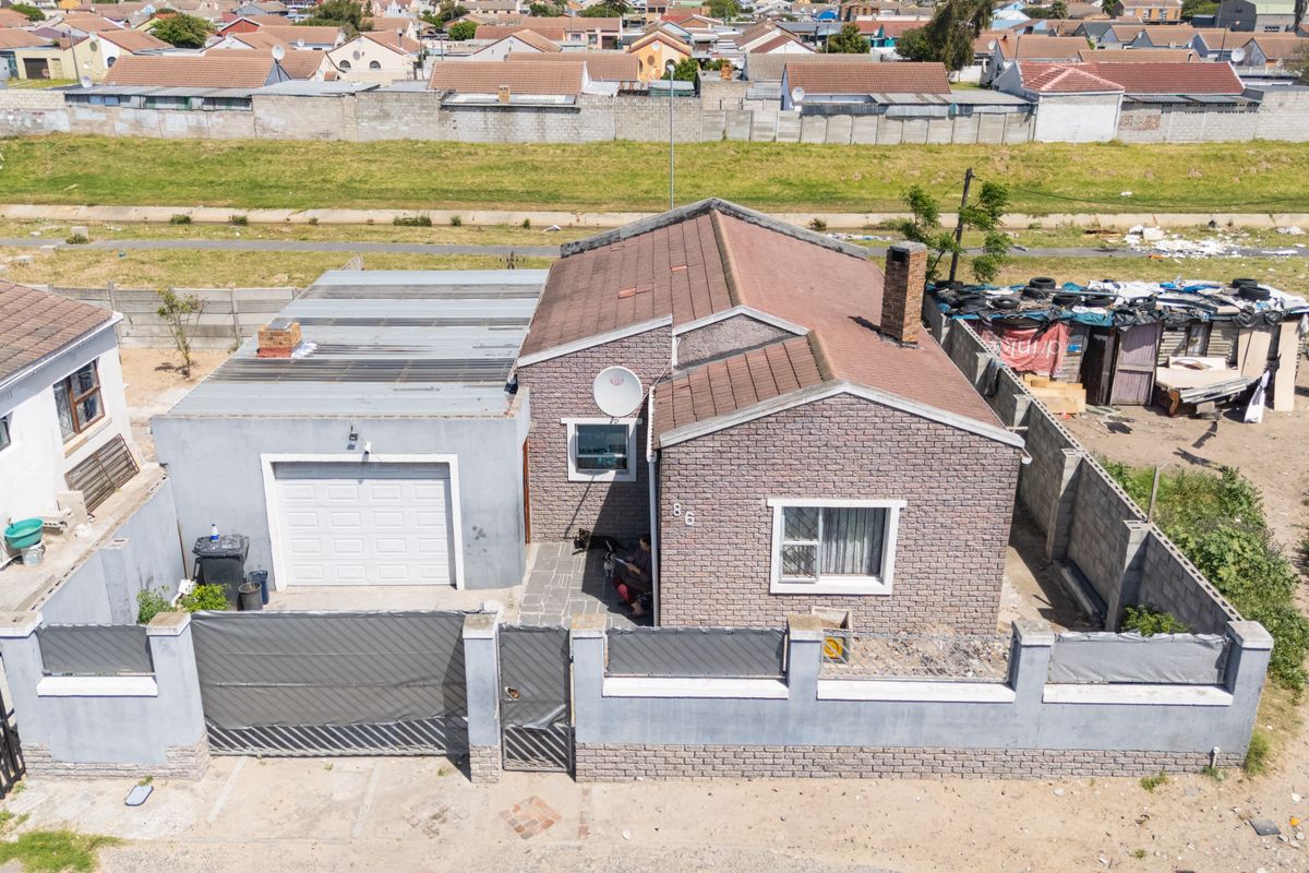 Aerial view of a detached brick house featuring a tiled roof, attached garage, and perimeter walling in a residential neighborhood setting.