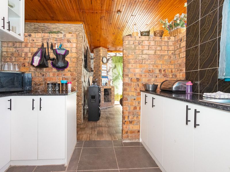 Kitchen featuring exposed brick walls, timber ceiling, granite countertops, and modern white cabinetry, offering a rustic yet functional cooking space.