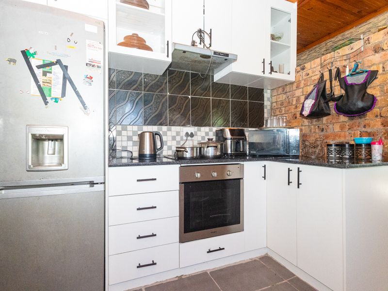 Compact kitchen featuring white cabinetry, granite countertops, a built-in oven, extractor fan, and a rustic exposed brick wall with timber ceiling accents.