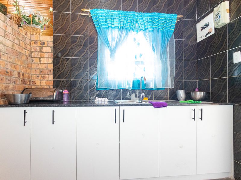 A functional kitchen area featuring white cabinetry, a granite countertop, and a stainless steel sink with dark tiled splashbacks.