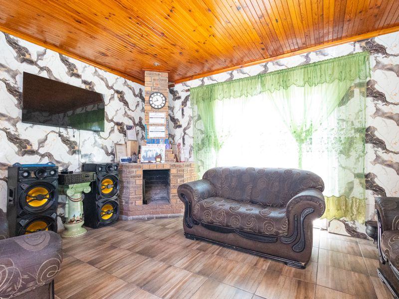 Living room featuring a brick fireplace, timber ceiling, and tiled flooring, offering a traditional aesthetic with potential for modern updates.