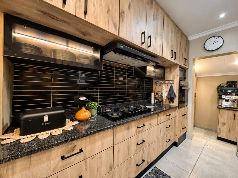 Modern kitchen featuring wood-grain cabinetry, black granite countertops, a gas hob with extractor fan, and a sleek black subway tile backsplash.