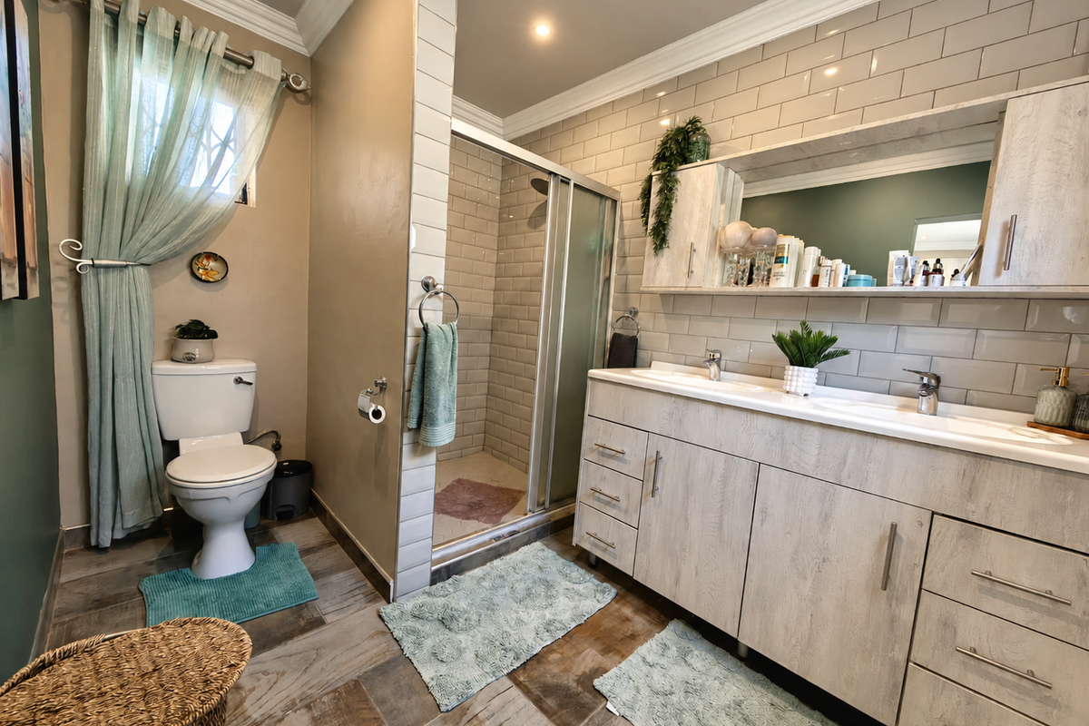 A well-maintained bathroom featuring a double vanity with wood-grain cabinetry, a glass-enclosed shower, and classic subway tile wall finishes.