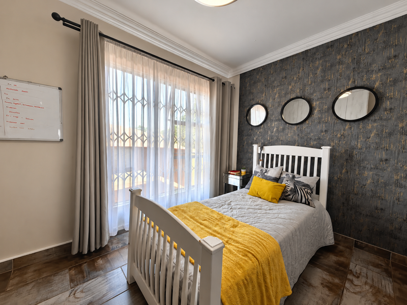 A well-maintained bedroom featuring tiled flooring, a textured accent wall, and a large window fitted with a security gate and curtain rod.