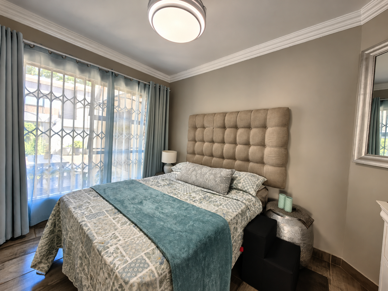 A well-maintained bedroom featuring crown molding, tiled flooring, and a large window with an integrated security gate.