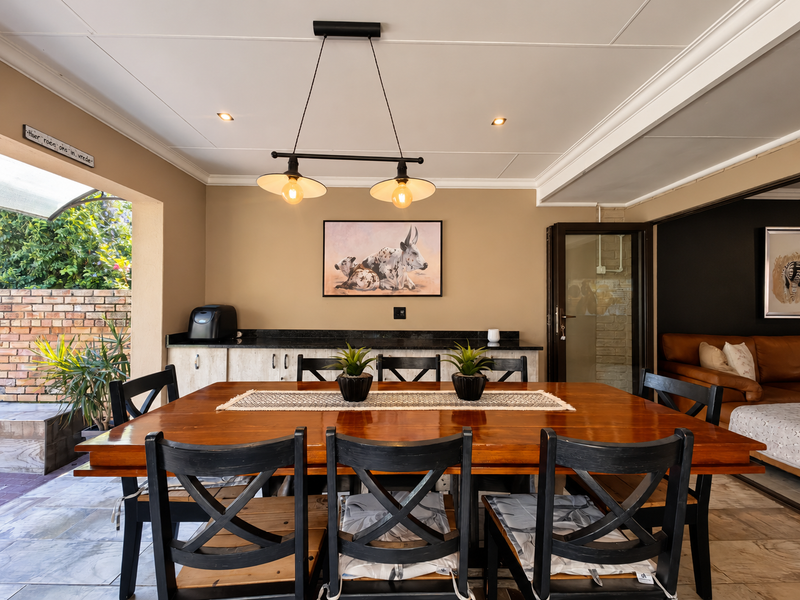 A well-maintained covered patio featuring built-in cabinetry with granite countertops, recessed and pendant lighting, and direct access to the garden area.