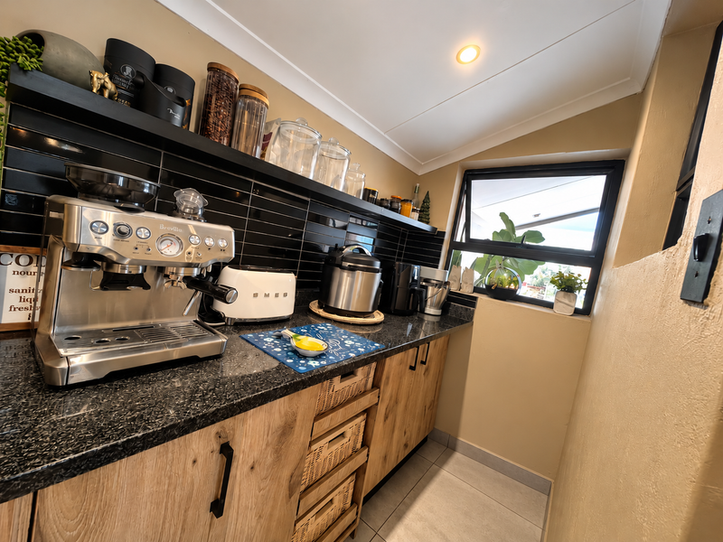 A compact and functional scullery featuring modern wood-look cabinetry, granite countertops, and a stylish black subway tile backsplash with ample built-in storage.