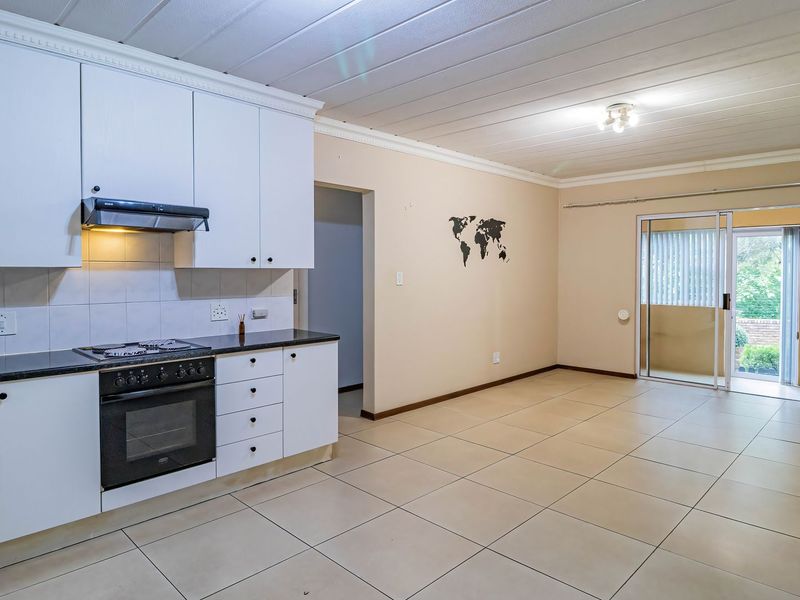 Open-plan kitchen and living area featuring white cabinetry, built-in oven and hob, tiled flooring, and sliding door access to an outdoor balcony.