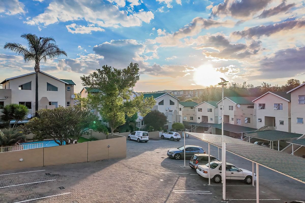 Aerial view of the apartment complex featuring a paved parking area with carports, a swimming pool, and well-maintained communal grounds at sunset.