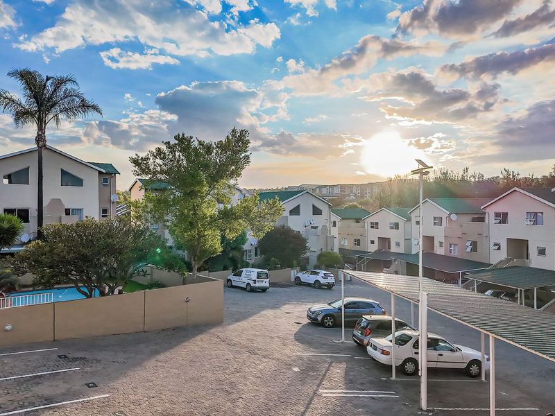 Aerial view of the apartment complex featuring a paved parking area with carports, a swimming pool, and well-maintained communal grounds at sunset.