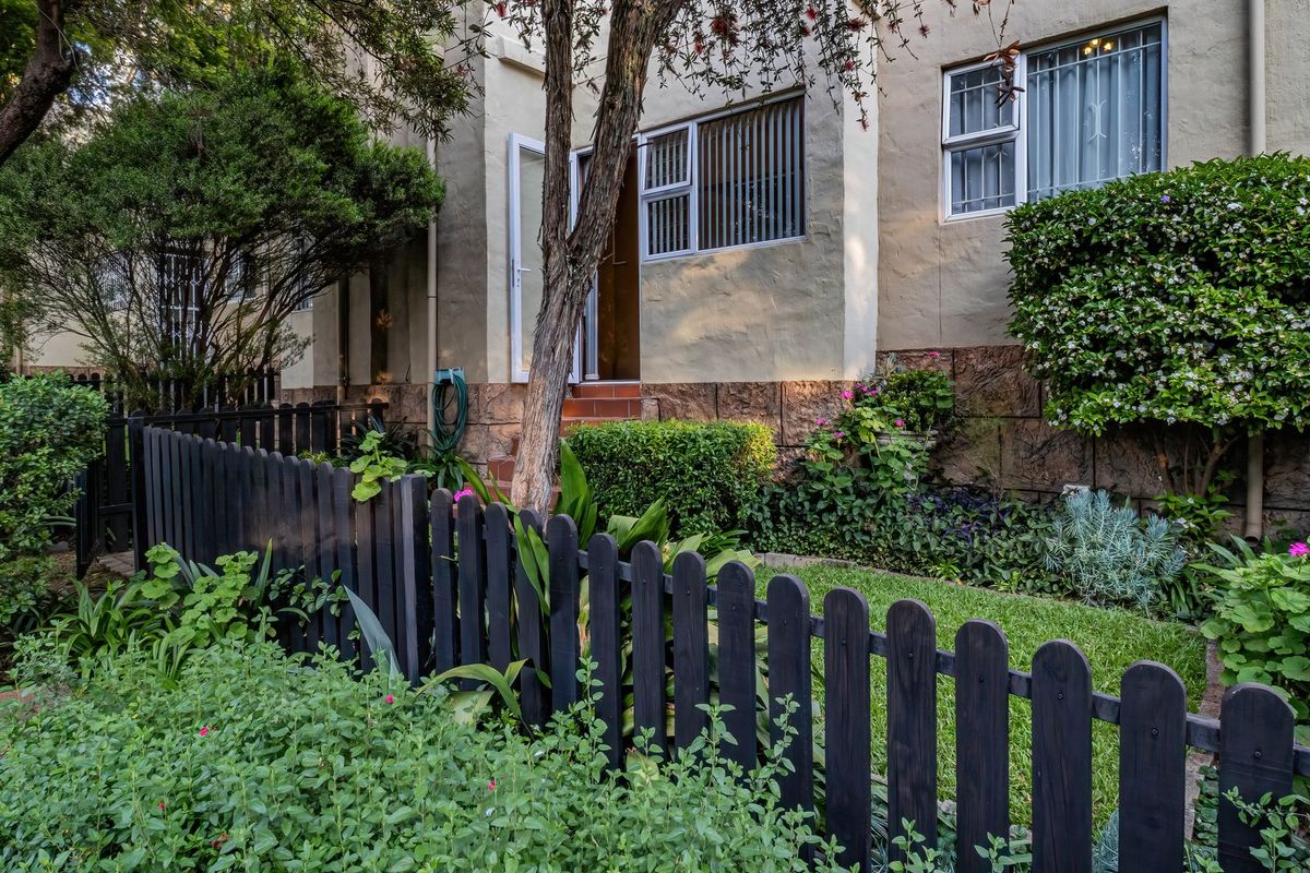 A view of the rear exterior of the apartment, featuring a private garden, stone-clad base, and secure window bars.