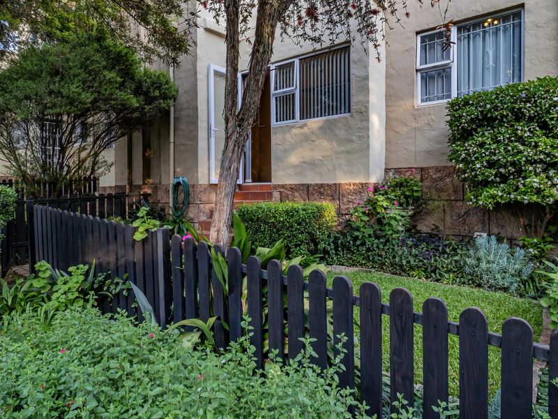 A view of the rear exterior of the apartment, featuring a private garden, stone-clad base, and secure window bars.