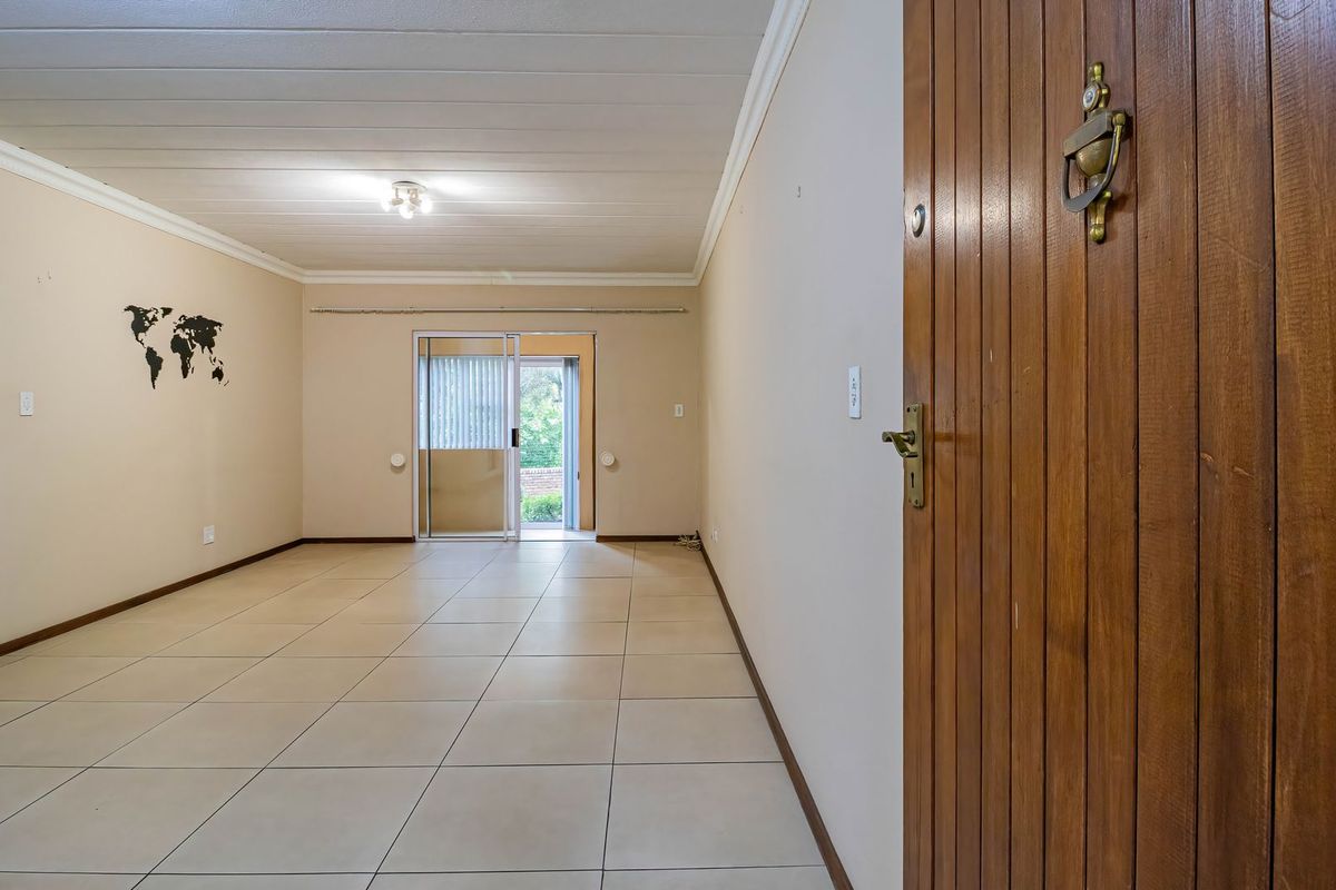 Spacious, empty living area featuring neutral tiled flooring, a timber entrance door, and a sliding glass door providing access to the exterior.