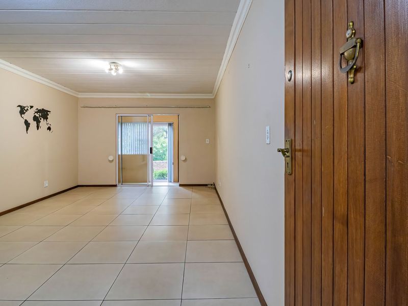 Spacious, empty living area featuring neutral tiled flooring, a timber entrance door, and a sliding glass door providing access to the exterior.