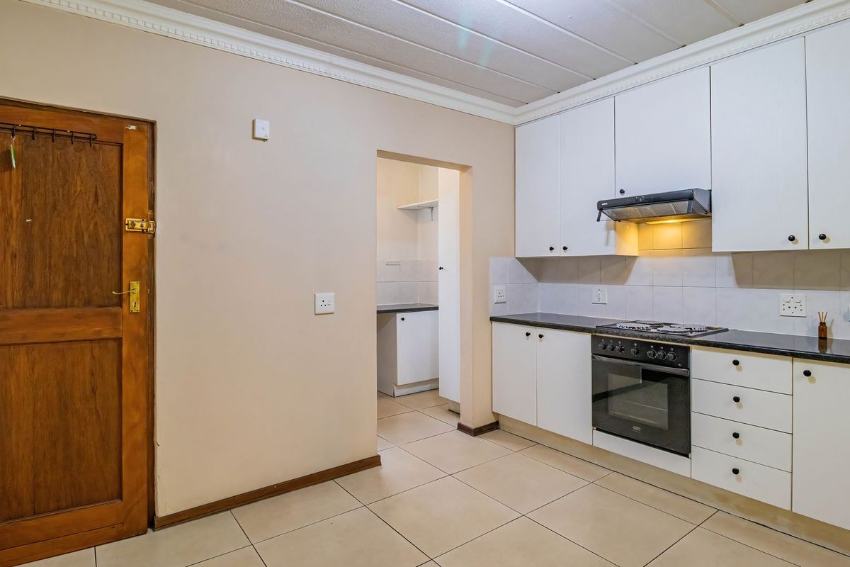 A functional kitchen featuring white cabinetry, dark countertops, built-in oven and hob, tiled flooring, and an adjacent scullery area.