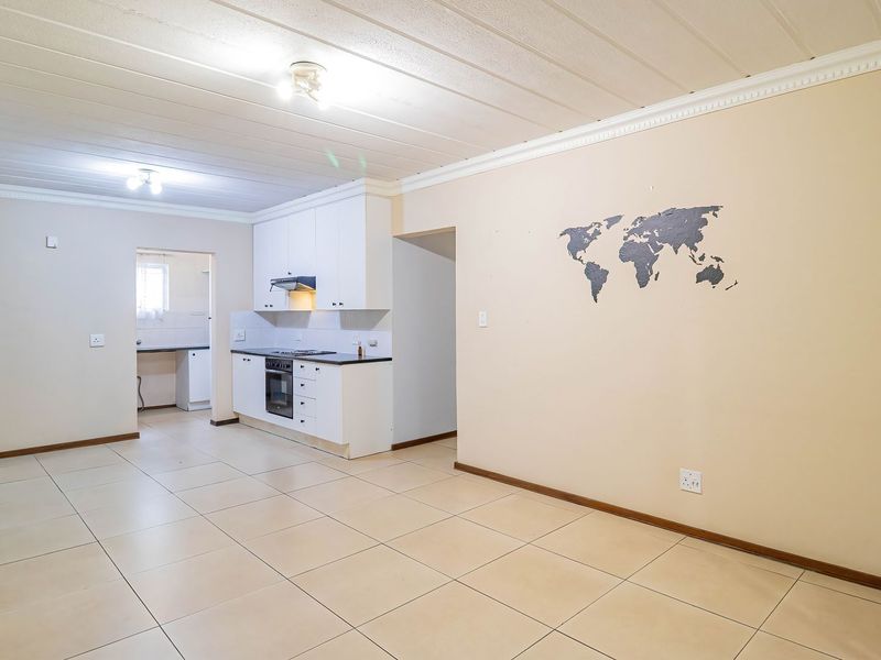 Spacious open-plan living area featuring tiled flooring, ceiling cornices, and a functional kitchen with built-in cabinetry, oven, and hob.