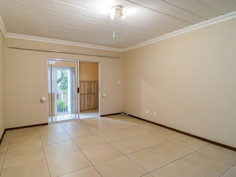 An empty living room featuring neutral tiled flooring, a sliding glass door leading to an outdoor area, and a simple ceiling light fixture.