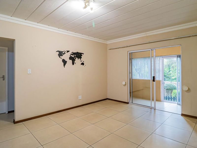 An empty living room featuring tiled flooring, a panelled ceiling with cornice detailing, and a sliding glass door providing access to an outdoor area.