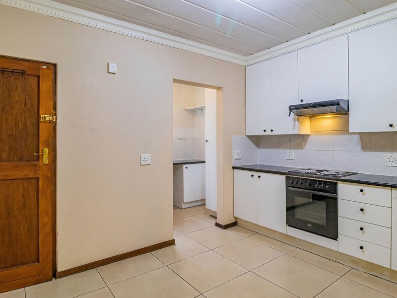 A functional kitchen featuring white cabinetry, dark countertops, built-in oven and hob, tiled flooring, and an adjacent scullery area.