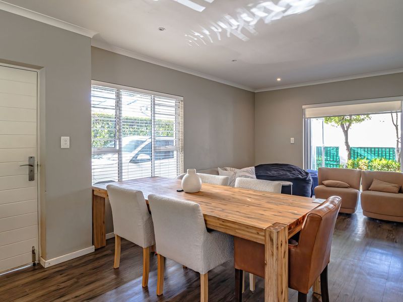Spacious open-plan living and dining area featuring durable laminate flooring, recessed lighting, and large windows with venetian blinds for natural light.