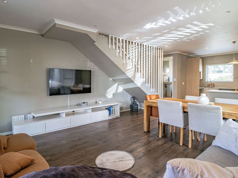 Spacious open-plan living and dining area featuring modern wooden flooring, a central staircase with balustrade, and a functional kitchen with integrated cabinetry.