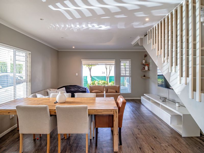 Spacious open-plan living and dining area featuring modern laminate flooring, a contemporary staircase with vertical balustrades, and a built-in media console.