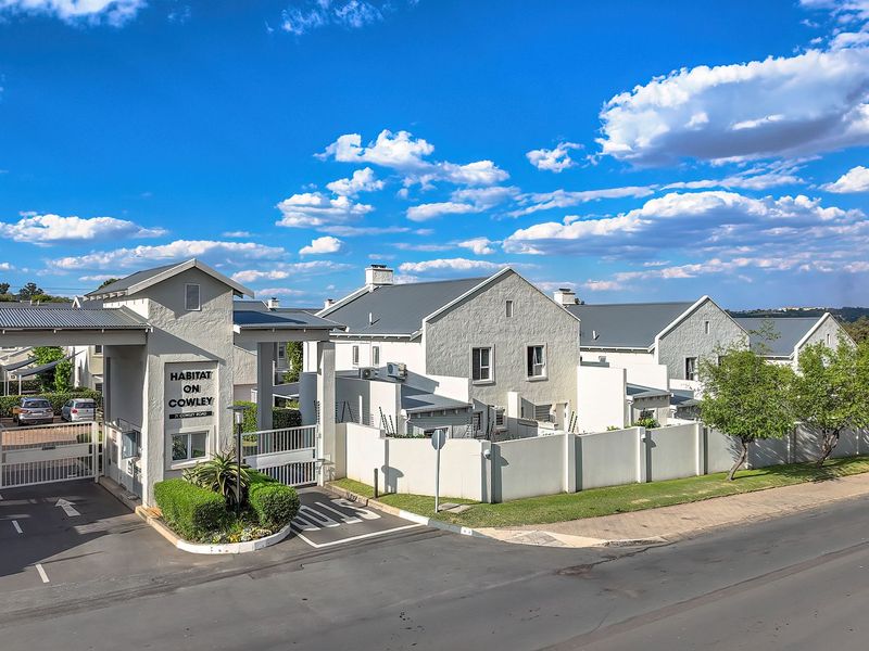 Aerial view of the secure entrance and front facade of the Habitat on Cowley townhouse complex, featuring gated access and well-maintained perimeter walls.