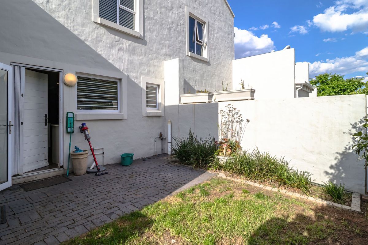 A private rear courtyard featuring a paved patio area, a small lawn, and secure boundary walls, providing a low-maintenance outdoor space.